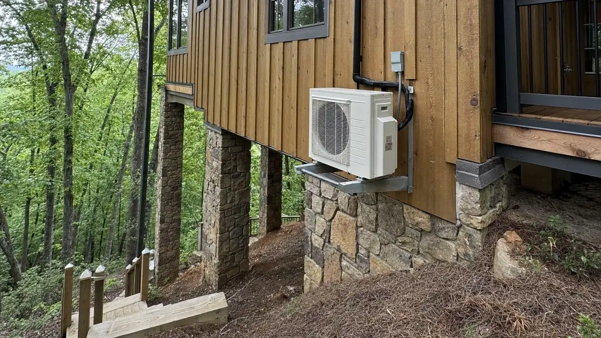 A heat pump condenser bracket-mounted on the lower elevation of a steep Bent Tree lot outside Jasper, Georgia