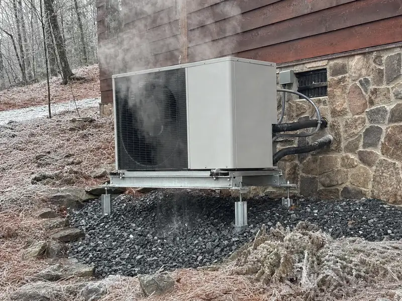 A condenser raised on a stand with positive drainage in a damp hollow, keeping defrost meltwater from freezing around the base