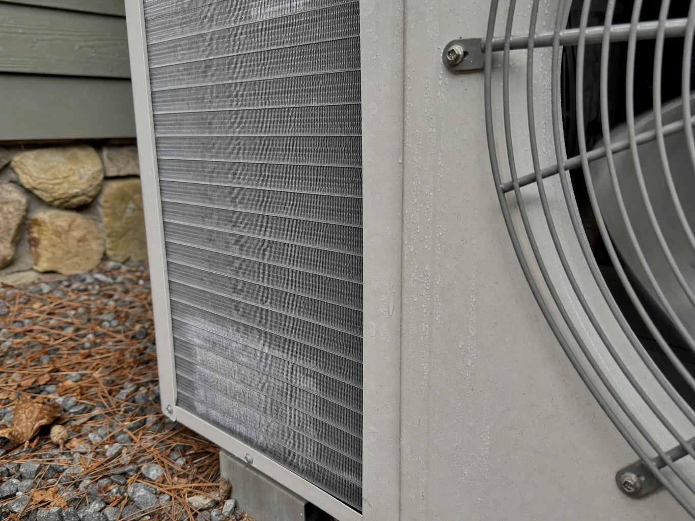 Close detail of a cold-climate condenser's coil fins and inverter fan during winter operation in the Pickens County mountains