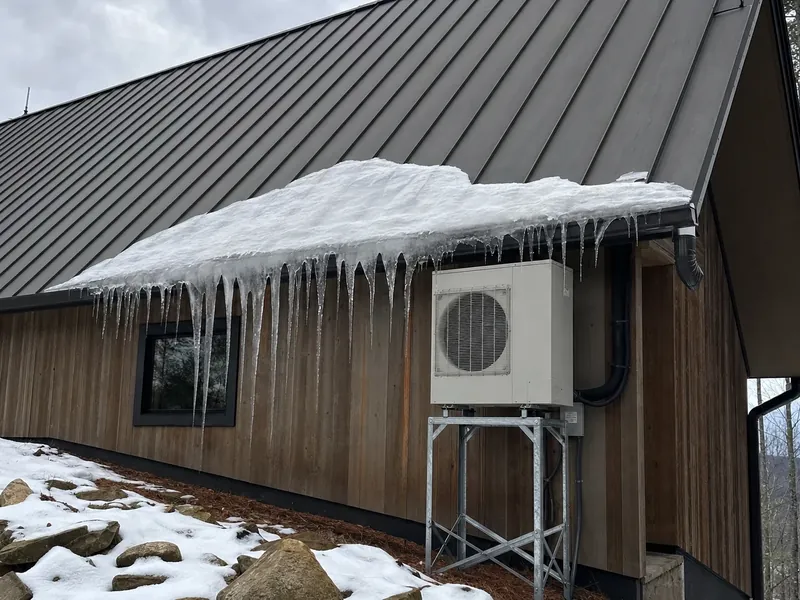 Ice sliding from a metal roof above an elevated condenser mount, the clearance detail that decides whether equipment survives a mountain winter