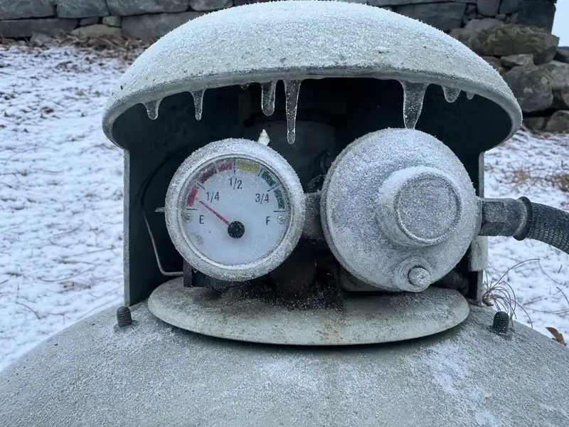 A propane tank gauge sitting near empty in deep winter, the run-out that forces a mandatory leak and pressure test before refill